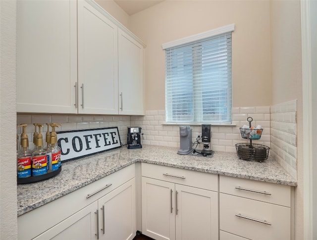 kitchen featuring tasteful backsplash, light stone counters, and white cabinets