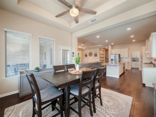 dining space featuring a tray ceiling, ceiling fan, dark wood-type flooring, and sink