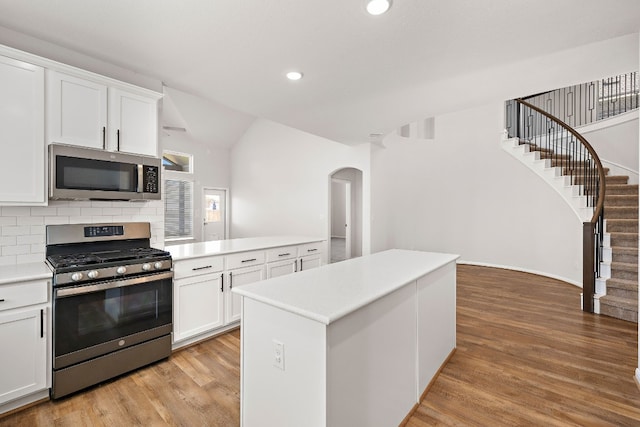 kitchen with white cabinets, light hardwood / wood-style flooring, appliances with stainless steel finishes, a center island, and decorative backsplash