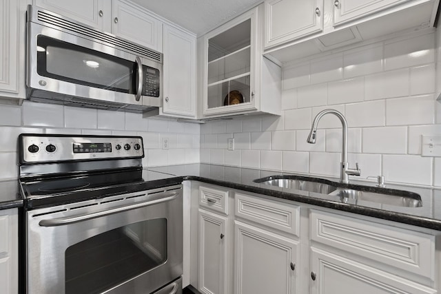 kitchen featuring white cabinetry, sink, stainless steel appliances, dark stone counters, and decorative backsplash