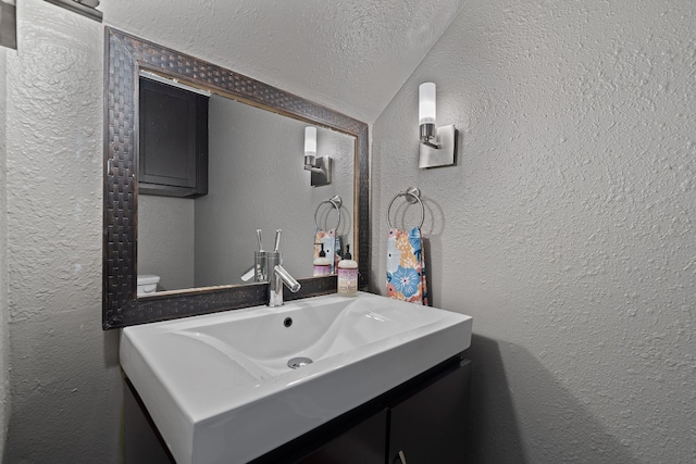 bathroom with vanity, a textured ceiling, vaulted ceiling, and toilet