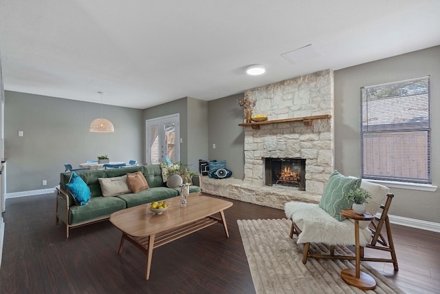 living room featuring a stone fireplace and dark wood-type flooring