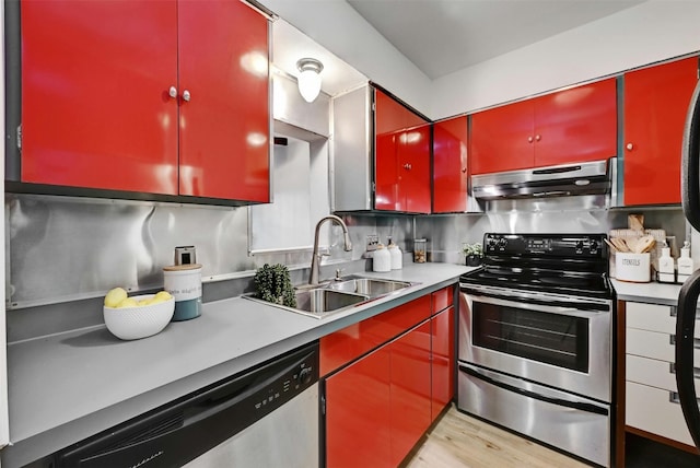 kitchen featuring under cabinet range hood, a sink, light countertops, appliances with stainless steel finishes, and red cabinets