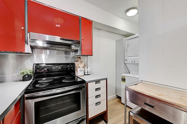 kitchen featuring red cabinets, light wood-style flooring, under cabinet range hood, stainless steel range with electric cooktop, and stacked washing maching and dryer