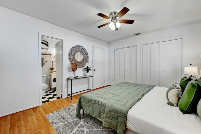 bedroom with two closets, visible vents, ensuite bathroom, ceiling fan, and light wood-type flooring