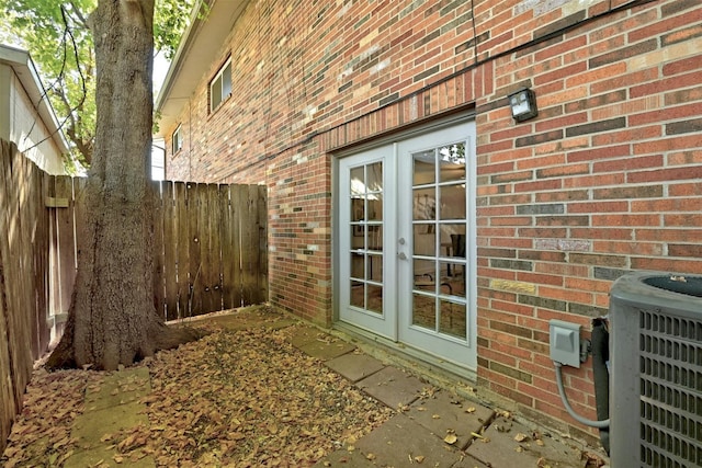 view of home's exterior with french doors, brick siding, fence, and central AC unit