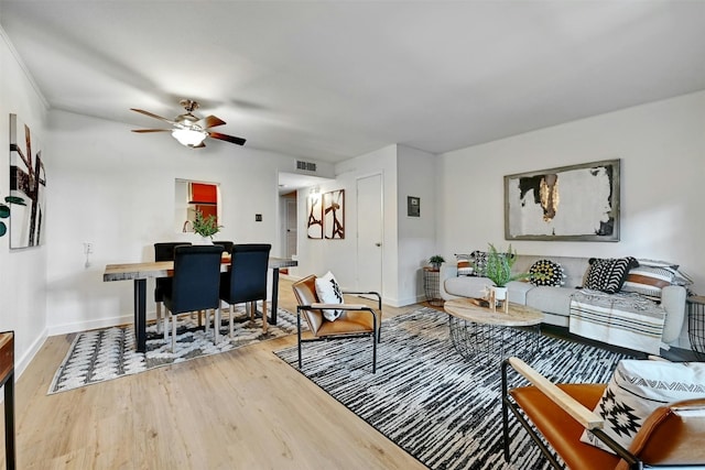 living room with light wood-style floors, baseboards, visible vents, and ceiling fan