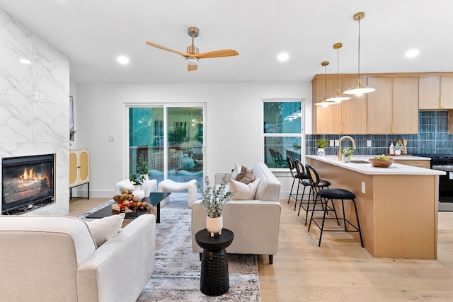 living room with a premium fireplace, light hardwood / wood-style flooring, sink, and ceiling fan