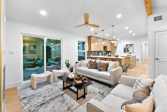 living room featuring light hardwood / wood-style floors, beamed ceiling, and ceiling fan