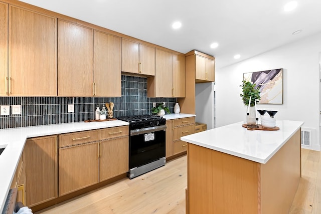 kitchen with light hardwood / wood-style flooring, stainless steel range with gas cooktop, a center island, and backsplash