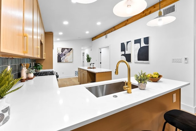 kitchen featuring tasteful backsplash, sink, kitchen peninsula, hanging light fixtures, and light hardwood / wood-style floors