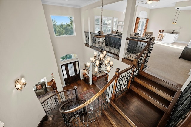 stairway with a towering ceiling, ornamental molding, wood finished floors, baseboards, and ceiling fan with notable chandelier