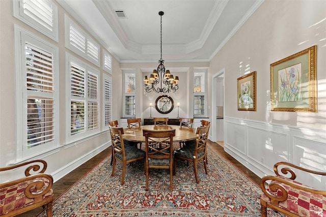 dining room with a tray ceiling, a wainscoted wall, dark wood finished floors, visible vents, and ornamental molding