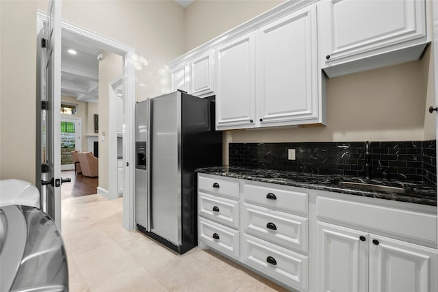 kitchen featuring a sink, stainless steel fridge, white cabinetry, and dark stone countertops