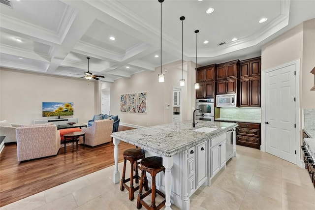 kitchen with decorative light fixtures, a spacious island, stainless steel microwave, open floor plan, and a kitchen breakfast bar