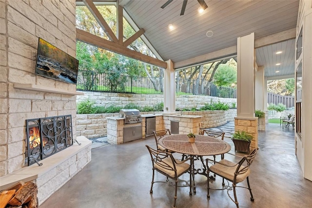 view of patio featuring ceiling fan, a fenced backyard, grilling area, exterior kitchen, and an outdoor stone fireplace