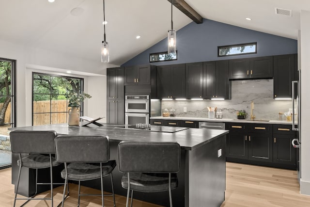 kitchen featuring decorative backsplash, black electric stovetop, pendant lighting, a center island with sink, and light hardwood / wood-style flooring