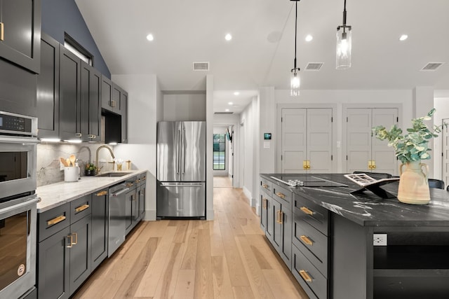 kitchen with sink, stainless steel appliances, dark stone counters, pendant lighting, and light hardwood / wood-style floors