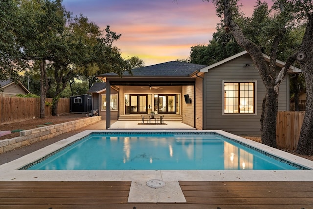 pool at dusk with a patio and ceiling fan