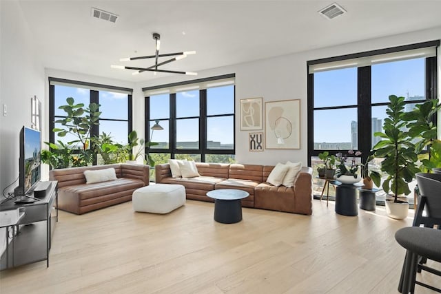 living area with light wood finished floors, visible vents, and an inviting chandelier