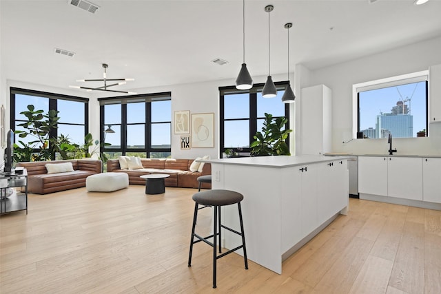 kitchen with sink, light hardwood / wood-style flooring, white cabinets, a center island, and hanging light fixtures