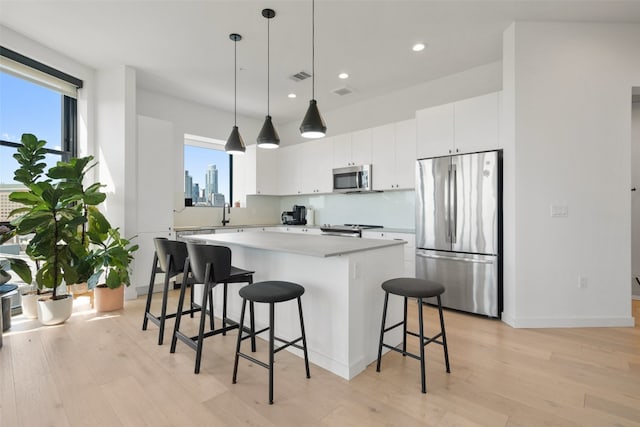 kitchen with decorative light fixtures, white cabinetry, stainless steel appliances, and a wealth of natural light