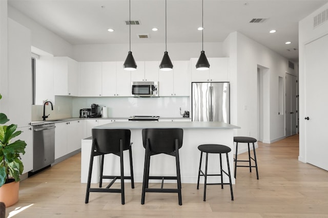 kitchen with white cabinetry, a center island, stainless steel appliances, light hardwood / wood-style flooring, and decorative light fixtures