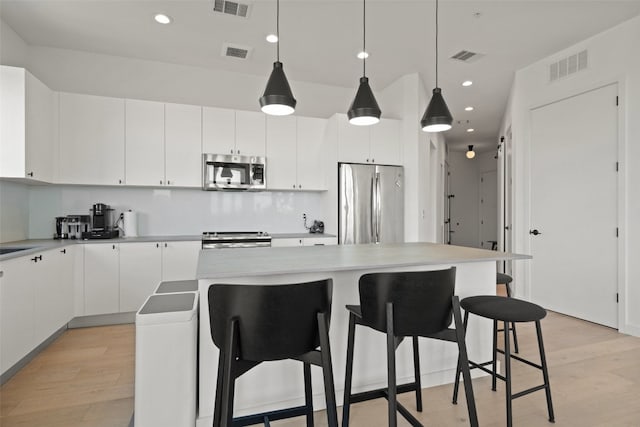 kitchen featuring stainless steel appliances, light hardwood / wood-style flooring, white cabinets, a center island, and hanging light fixtures