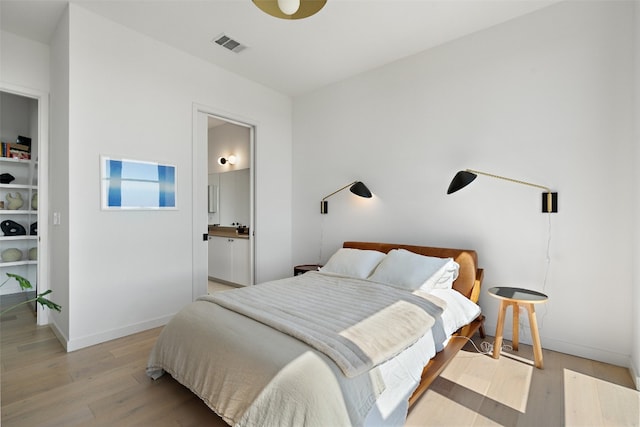 bedroom with ensuite bath and light hardwood / wood-style flooring