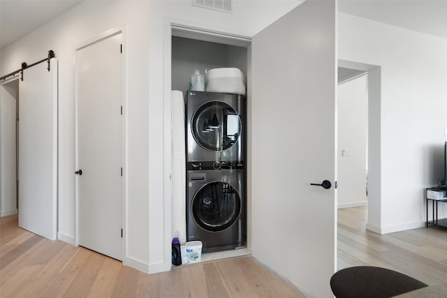 laundry room featuring a barn door, stacked washing maching and dryer, and light hardwood / wood-style floors