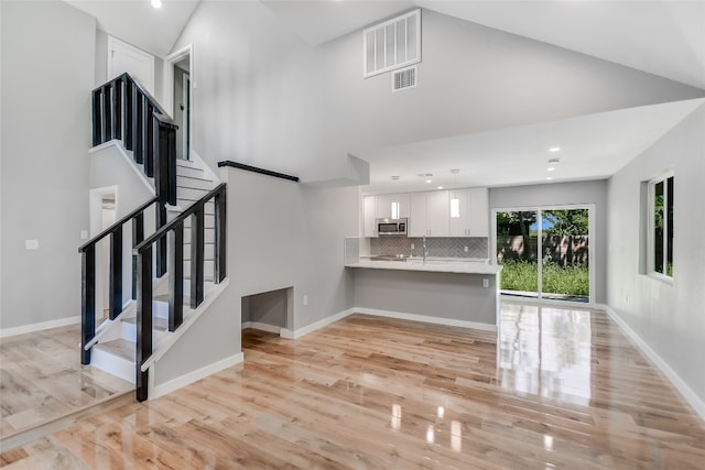 unfurnished living room with light wood-type flooring and high vaulted ceiling