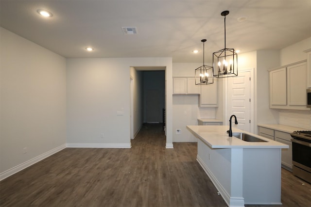 kitchen with pendant lighting, appliances with stainless steel finishes, an island with sink, sink, and dark hardwood / wood-style floors