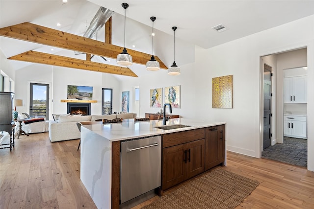 kitchen featuring light wood-type flooring, a kitchen island with sink, sink, decorative light fixtures, and stainless steel dishwasher