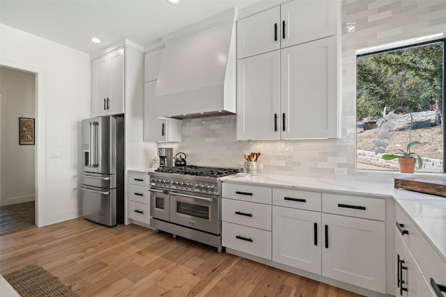 kitchen with premium appliances, a wealth of natural light, white cabinetry, and premium range hood