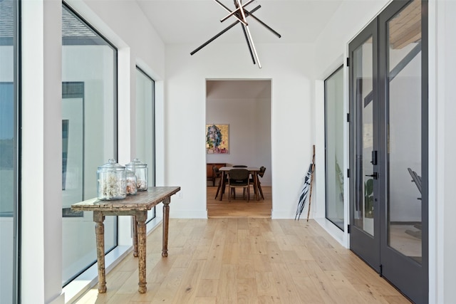 hall with light wood-type flooring, a healthy amount of sunlight, and an inviting chandelier