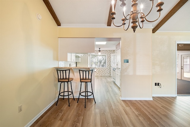 dining room with light hardwood / wood-style flooring, a chandelier, beamed ceiling, and ornamental molding