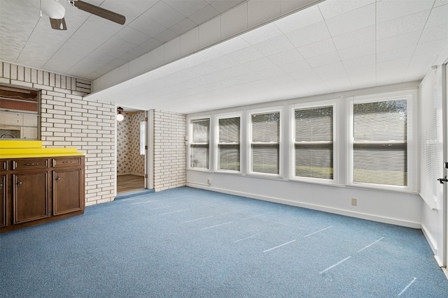 unfurnished living room featuring carpet, ceiling fan, and brick wall