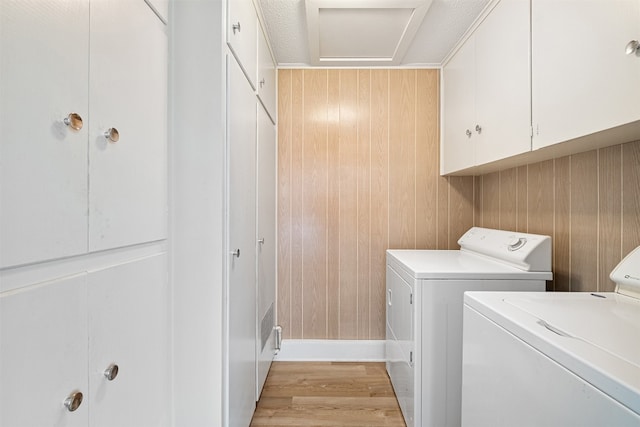 clothes washing area featuring cabinets, light wood-type flooring, wood walls, and washer and clothes dryer