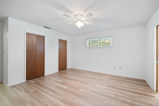 unfurnished bedroom featuring a textured ceiling, light hardwood / wood-style floors, ceiling fan, and multiple closets