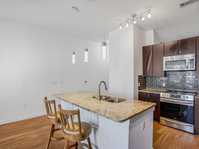 kitchen with sink, decorative light fixtures, a kitchen island with sink, dark brown cabinets, and appliances with stainless steel finishes