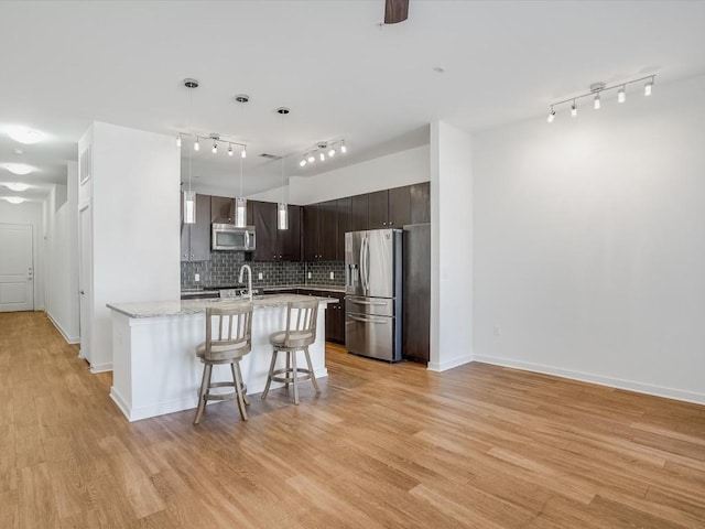 kitchen featuring decorative light fixtures, a breakfast bar area, dark brown cabinets, appliances with stainless steel finishes, and light wood-type flooring