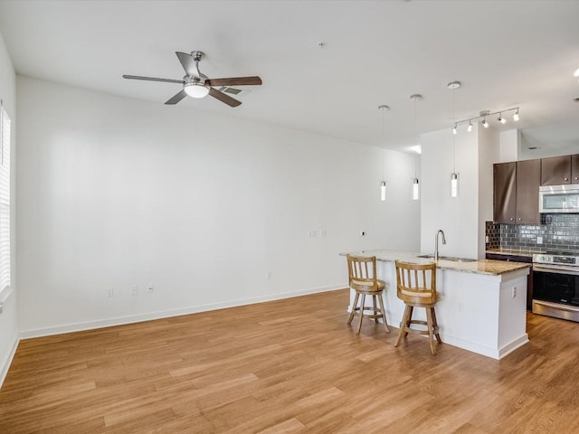 kitchen with decorative backsplash, appliances with stainless steel finishes, sink, light hardwood / wood-style floors, and an island with sink