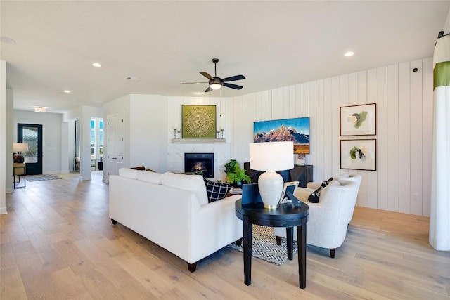 living room featuring a tile fireplace, light wood-type flooring, ceiling fan, and wooden walls