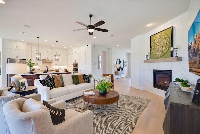 living room featuring sink, light hardwood / wood-style floors, ceiling fan, and a premium fireplace