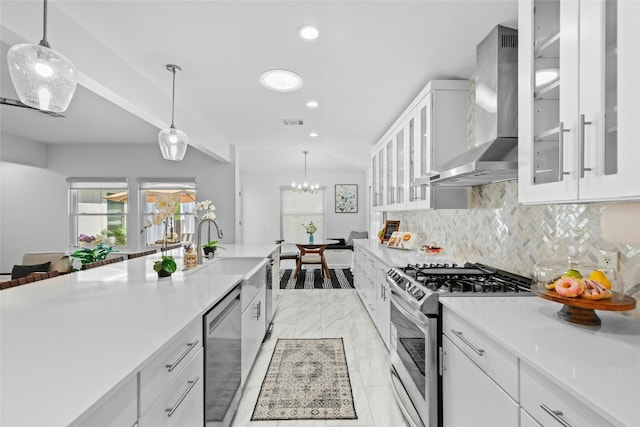 kitchen featuring pendant lighting, wall chimney exhaust hood, white cabinetry, and appliances with stainless steel finishes