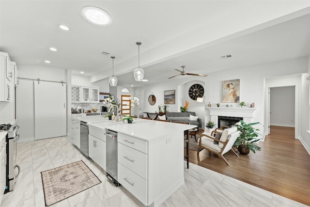 kitchen featuring decorative light fixtures, a fireplace, white cabinets, a center island with sink, and appliances with stainless steel finishes