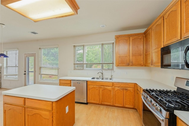 kitchen with light wood-type flooring, appliances with stainless steel finishes, a kitchen island, and sink