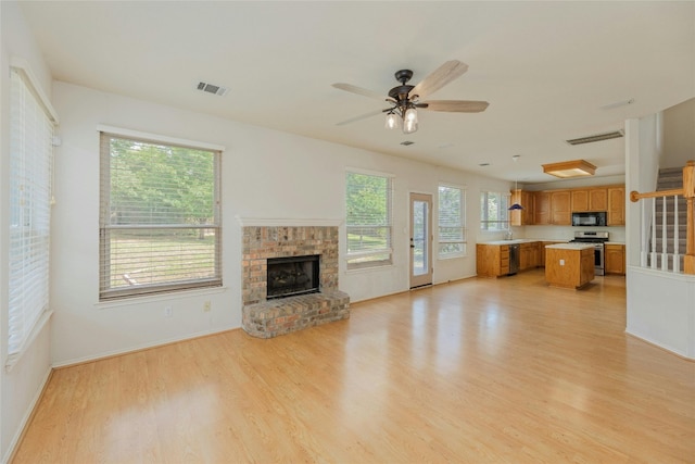 unfurnished living room with light hardwood / wood-style flooring, a brick fireplace, and ceiling fan