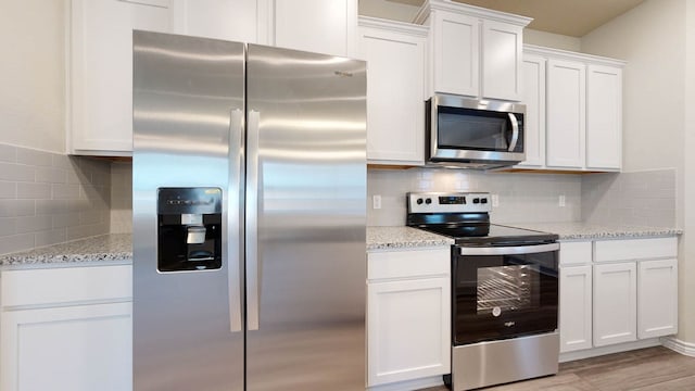 kitchen featuring white cabinets, backsplash, light stone countertops, stainless steel appliances, and light wood-type flooring