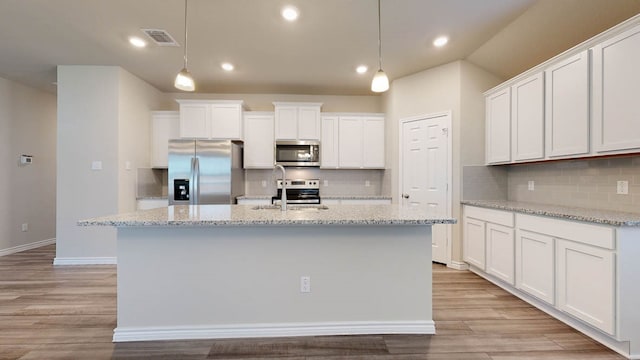 kitchen with white cabinets, a center island with sink, light hardwood / wood-style flooring, decorative light fixtures, and appliances with stainless steel finishes